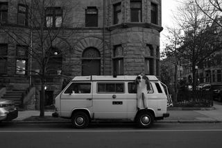 Vintage microbus with a wetsuit hanging off of it parked on street